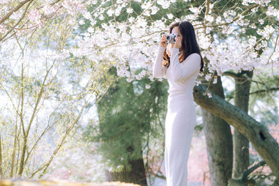 Portrait of young woman standing against trees