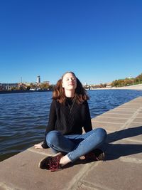 Beautiful young woman sitting at promenade against blue sky
