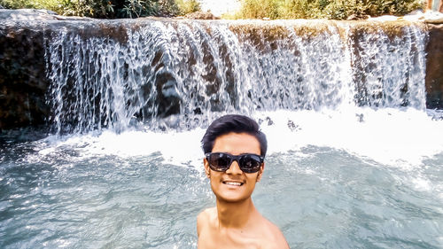 Portrait of man wearing sunglasses against waterfall