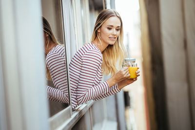 Young woman holding drink out of window