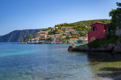 Buildings by sea against clear blue sky