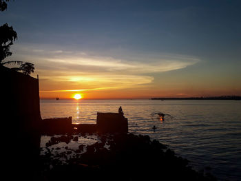 Silhouette people on beach against sky during sunset