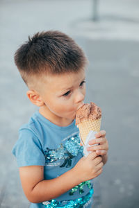 Cute boy eating ice cream cone while standing on road