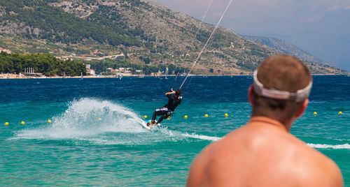 Rear view of male looking at man kiteboarding in sea