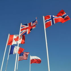 Low angle view of national flags waving against clear blue sky