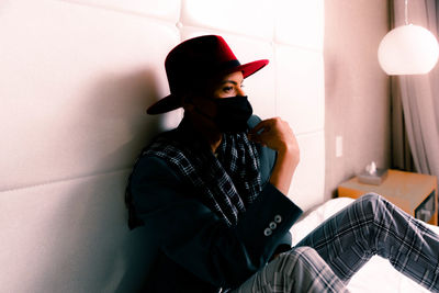 Full length of man sitting on bed against wall