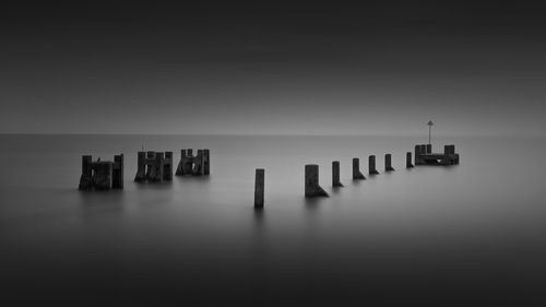 Wooden posts in sea against sky