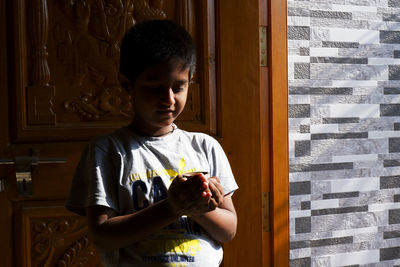 Cute boy holding cup standing by door