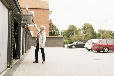 Senior woman holding garage door while standing by cars against clear sky
