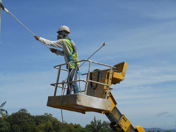 Low angle view of man standing on cherry picker against sky