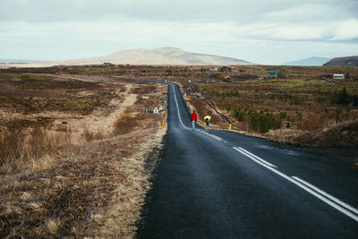 Rear view of couple skateboarding on road against sky