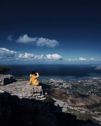 Man sitting on rock by sea against sky