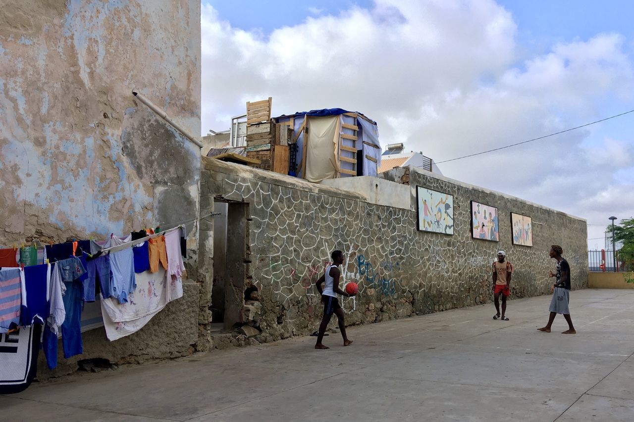 built structure, architecture, building exterior, sky, cloud - sky, group of people, real people, men, day, nature, women, lifestyles, people, full length, wall - building feature, city, building, walking, hanging, outdoors