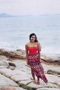 Portrait of smiling woman standing on rock at beach