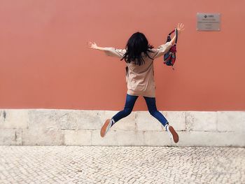 Rear view of excited woman jumping against coral wall