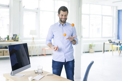 Smiling businessman juggling with tangerines in office