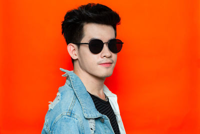 Portrait of young man wearing sunglasses against orange background