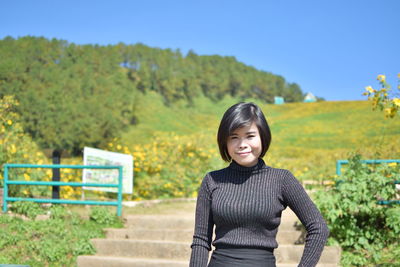 Portrait of smiling young woman standing against trees