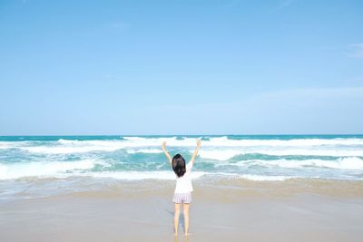 Rear view of woman standing at beach against sky