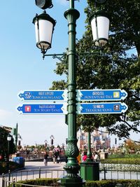 Road sign by street light against sky