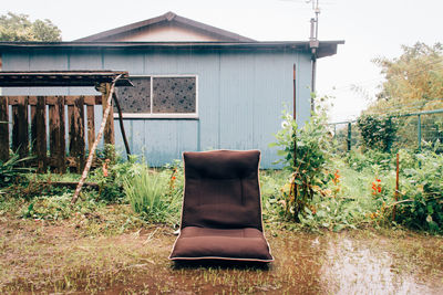 Empty seat in wet yard by house against clear sky