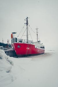 Boat moored on snow covered shore against sky
