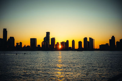 Silhouette buildings by sea against sky during sunset