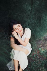 High angle view of woman with eyes closed sitting b y tree in forest