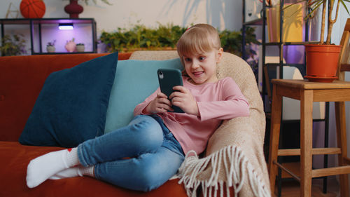 Girl using mobile phone sitting on sofa at home