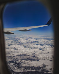 Airplane flying over snowcapped mountains against sky seen through window