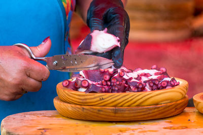 Midsection of female vendor slicing octopus through scissor at fish market