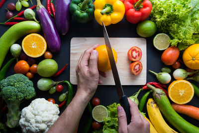 Cropped image of hands cutting fruit on board surrounded with vegetables