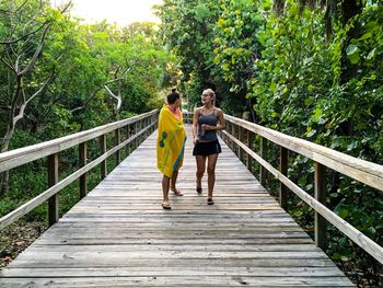 Female friends walking on wooden bridge amidst trees