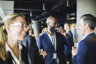 Smiling entrepreneur drinking black coffee while standing with colleagues in office