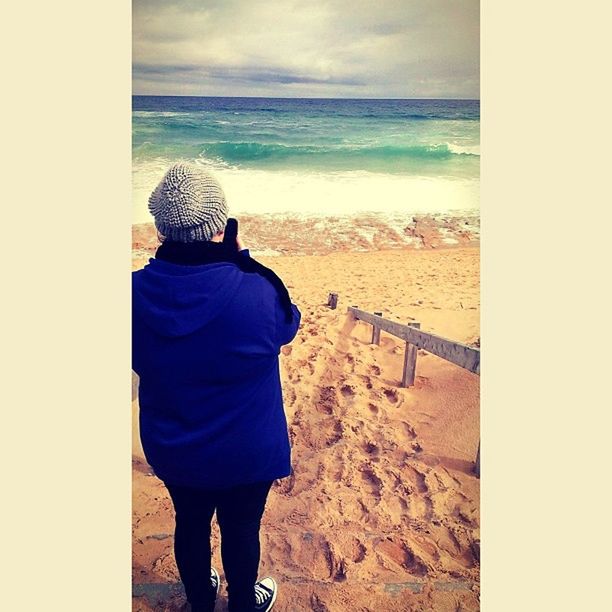 REAR VIEW OF MAN PHOTOGRAPHING SEA SHORE