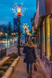 Rear view of woman walking on illuminated street at night