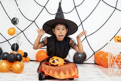 Full length of boy holding pumpkin against orange during halloween