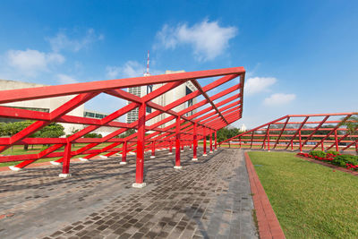 Red metallic structure on footpath against sky