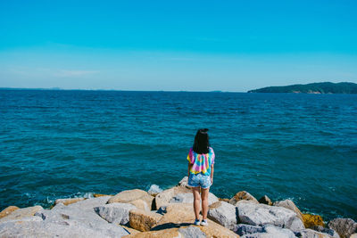 Rear view of girl standing against sea on rock