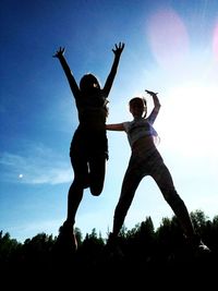 Low angle view of woman jumping against sky