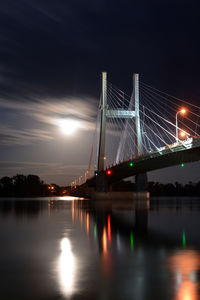 Illuminated bridge over river against sky at night