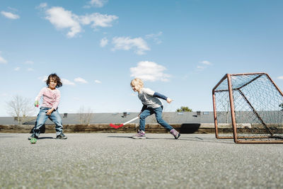 Children playing hockey at yard against blue sky