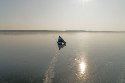 Boy at frozen lake against sky during sunset