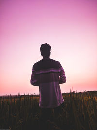 Rear view of man standing on field against sky during sunset