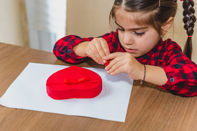 High angle view of girl making heart shape on paper at home