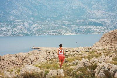 Rear view of woman walking on rocky riverbank by mountain