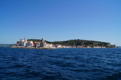 Buildings by sea against clear blue sky