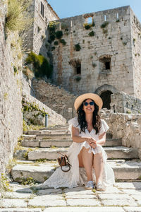 Front view of beautiful woman sitting on stone stairs in medieval fortress klis in split, croatia