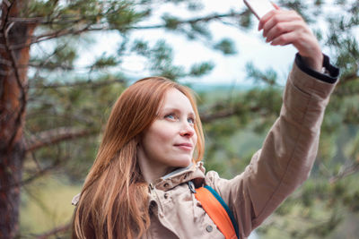 Woman taking selfie while standing against trees