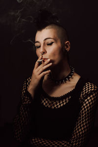 Young woman smoking cigarette against black background